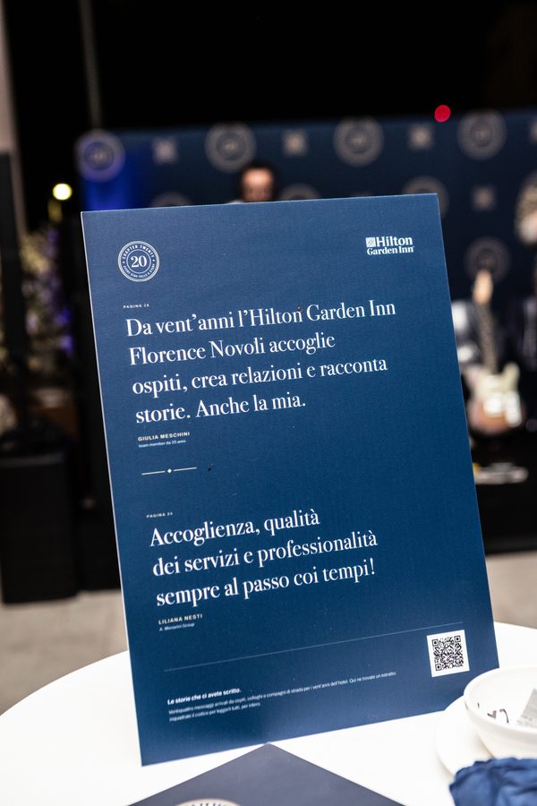 Un espositore della mostra con due messaggi degli ospiti e il QR, su un tavolino