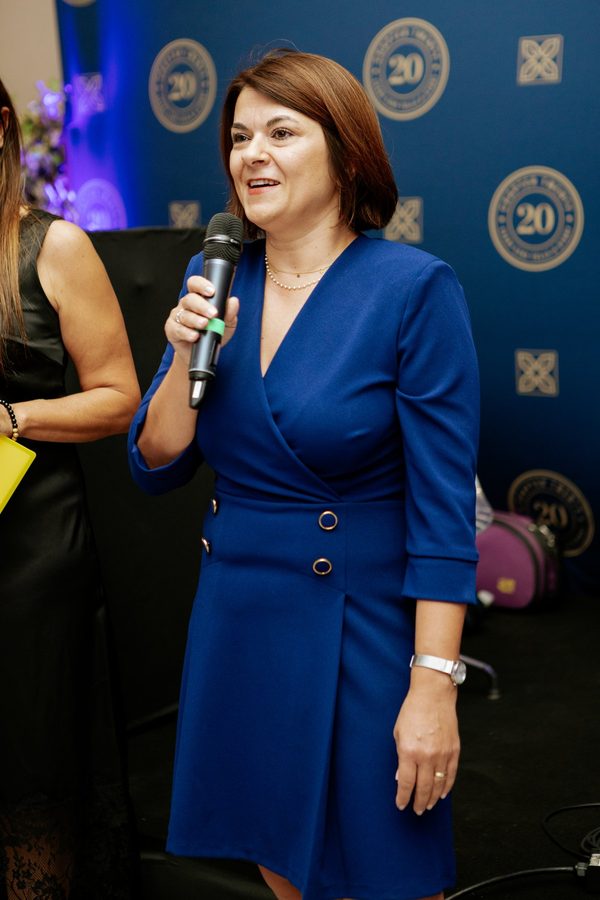 La direttrice Alina Grigoras al microfono, in abito blu, davanti al fondale coi sigilli