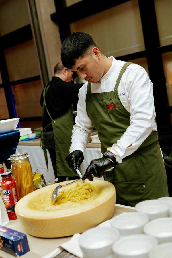 Un cuoco manteca la pasta fresca dentro una forma di formaggio