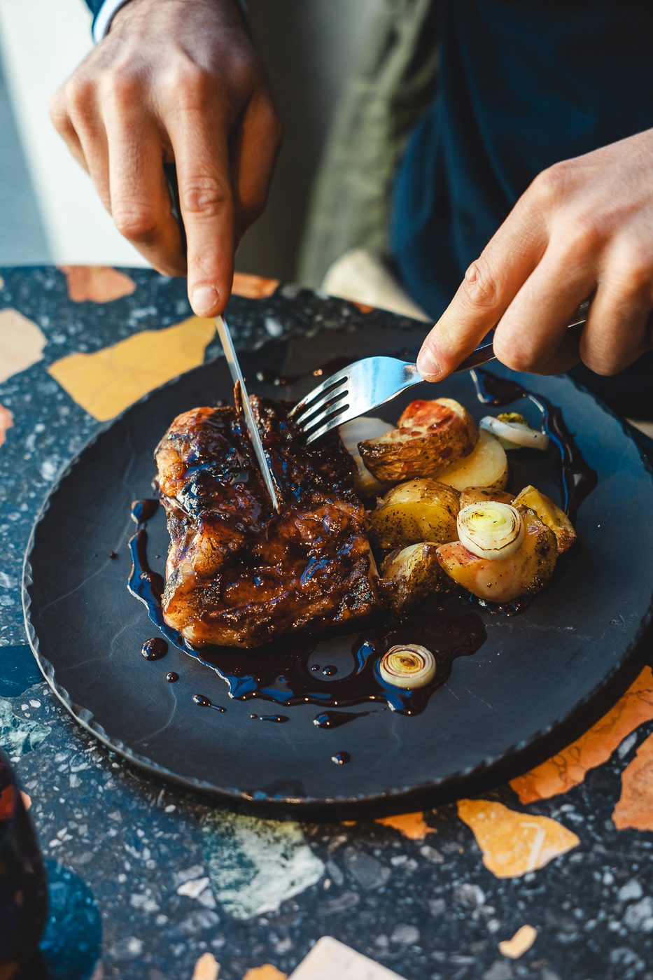 Due mani tagliano un piatto di carne su un tavolo in graniglia