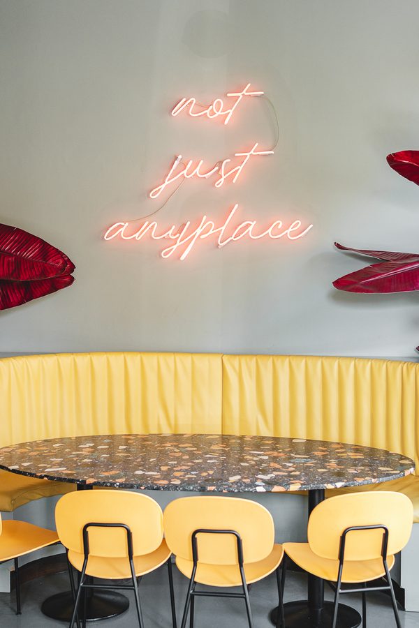 La scritta al neon «not just anyplace» sopra il divanetto giallo di Amedeo