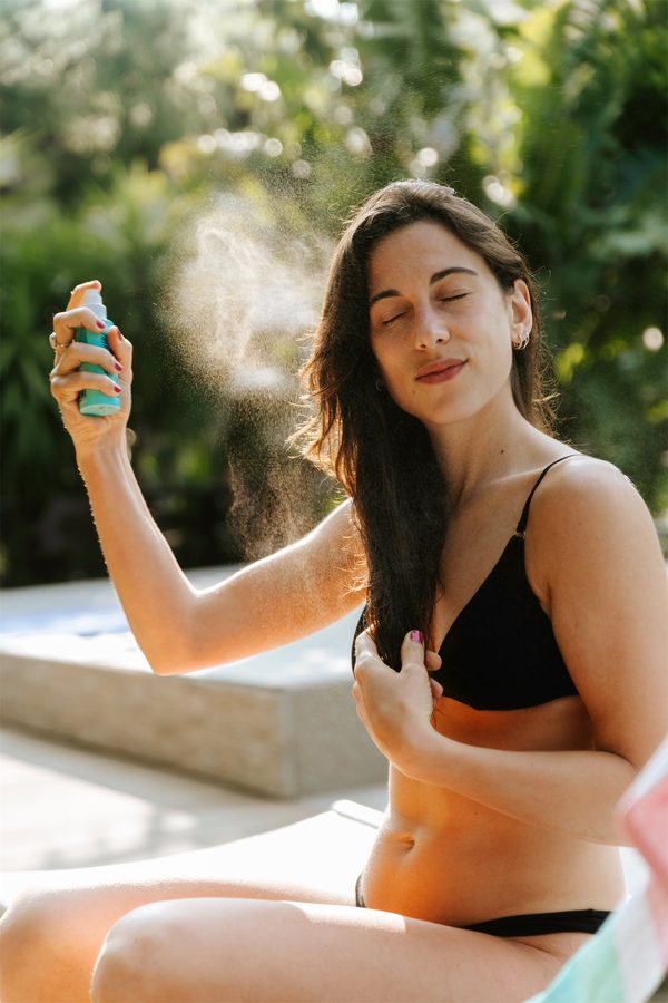 Una ragazza in costume si spruzza una nebbia sul viso, a bordo piscina