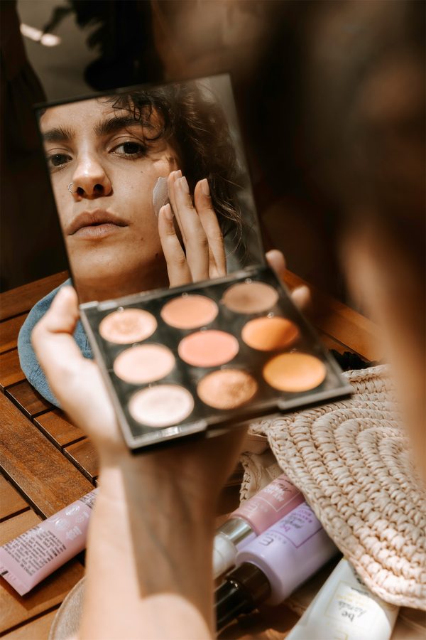 Una ragazza si trucca guardandosi in uno specchietto, con la palette in mano