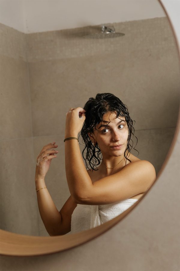 Una ragazza coi capelli bagnati si guarda nello specchio tondo del bagno