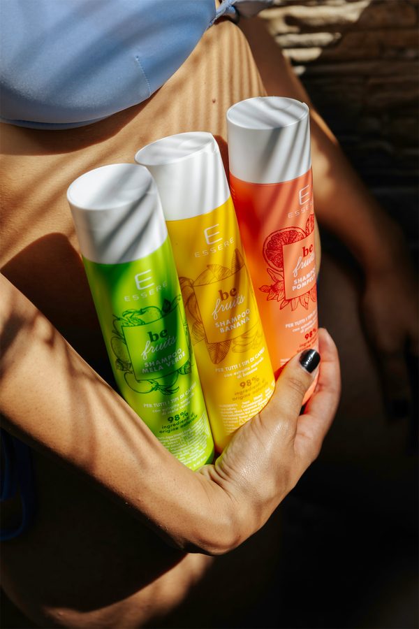 Due mani stringono al sole tre flaconi Essere Bio: verde, giallo e rosso