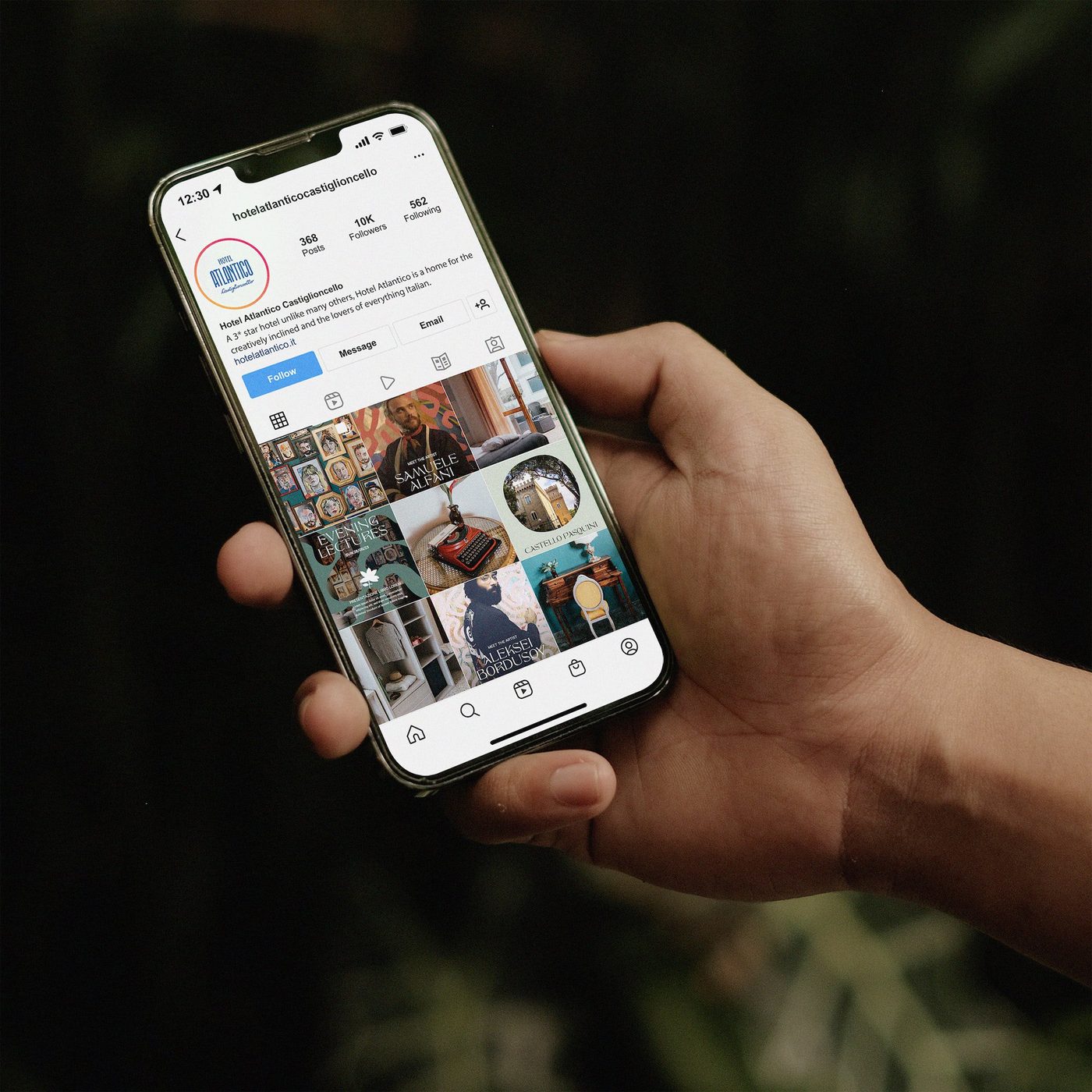 Una mano tiene un telefono col profilo Instagram dell’Hotel Atlantico