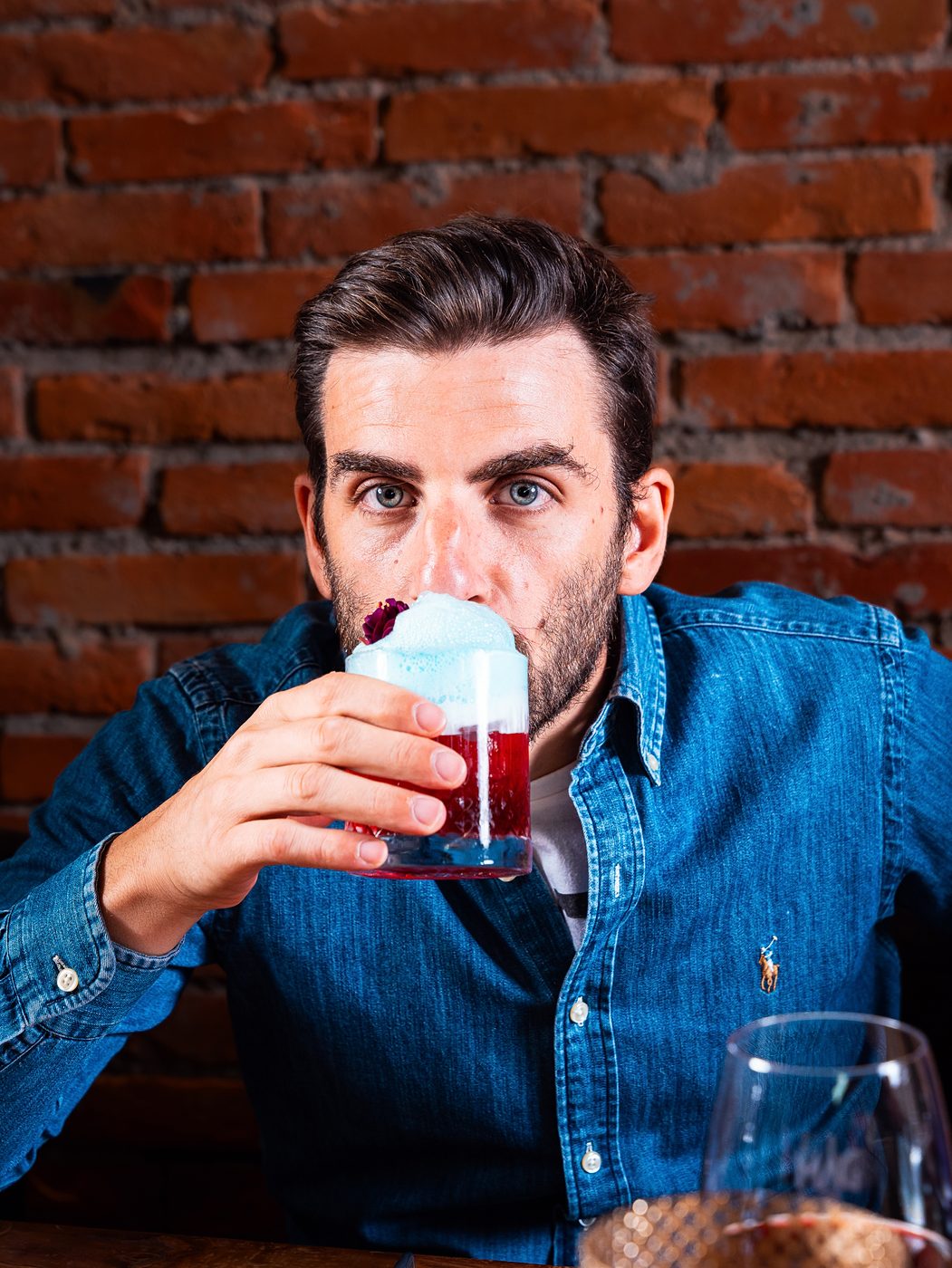 Un ragazzo in camicia di jeans beve un cocktail davanti al muro di mattoni