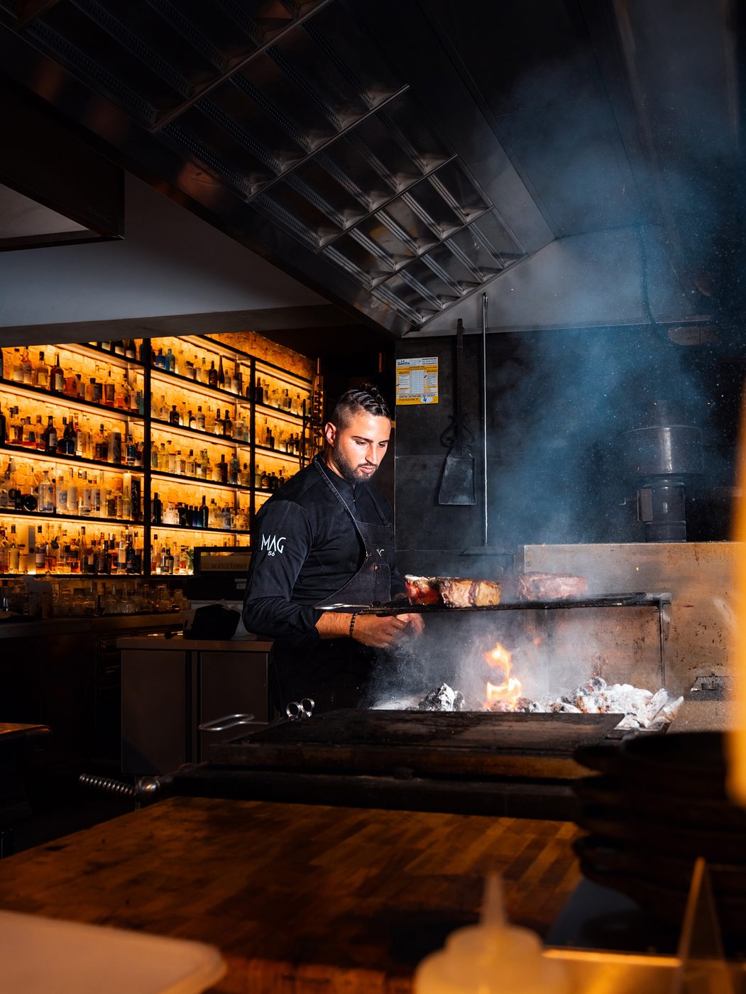 La cucina di MAG 56 con la griglia accesa e le bottiglie illuminate