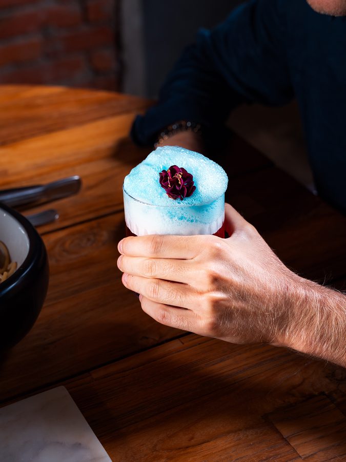 Una mano solleva un cocktail azzurro
