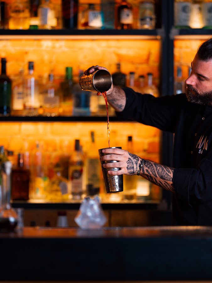 Il barman al lavoro davanti alla parete di bottiglie illuminate