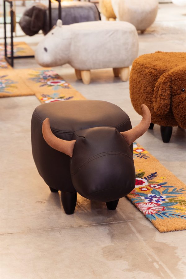 Uno sgabello a forma di toro accanto a un pouf di pelo