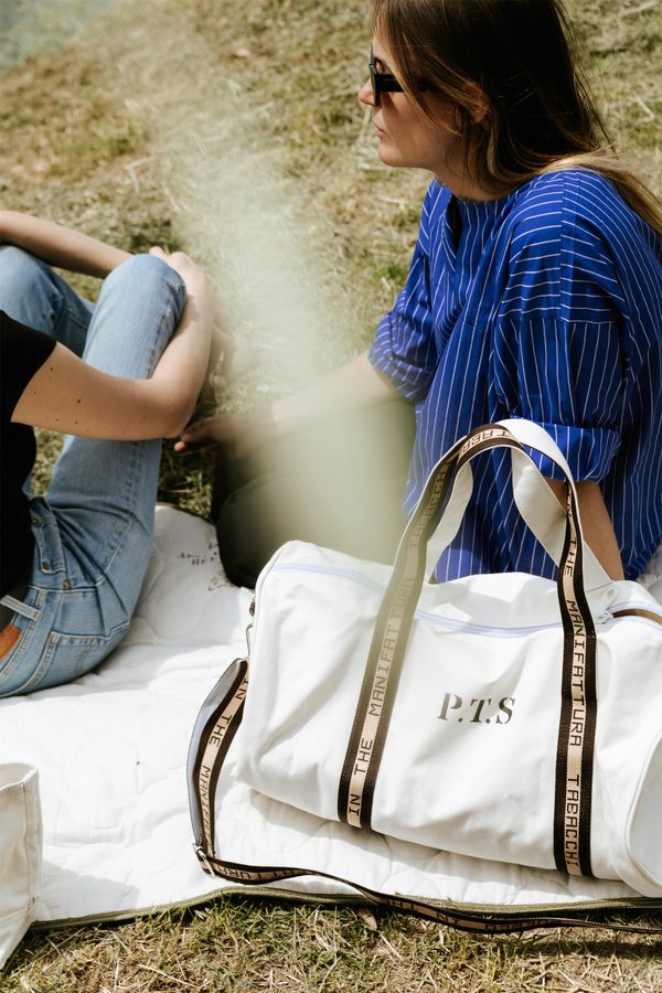 Una ragazza seduta sull’erba con una borsa bianca Puebco