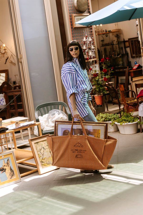 Una ragazza con la borsa Puebco in una bottega piena di quadri